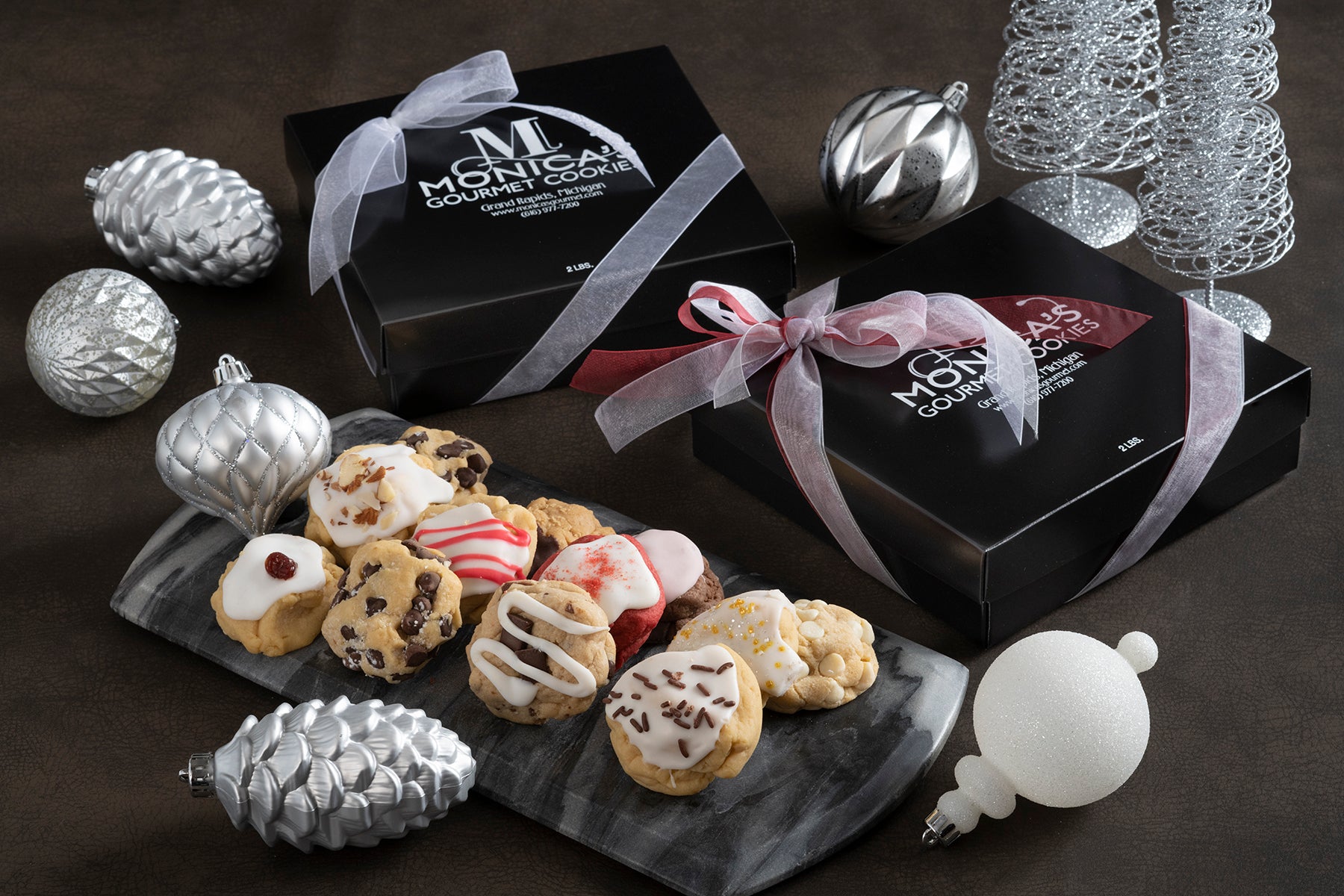 Our gourmet cookies boxes wrapped in holiday ribbon, with an assortment of holiday flavors, Amaretto, Caramel Rock, Chocolate Chip, Iced Sugar Gems, red Velvet, and Peppermint.