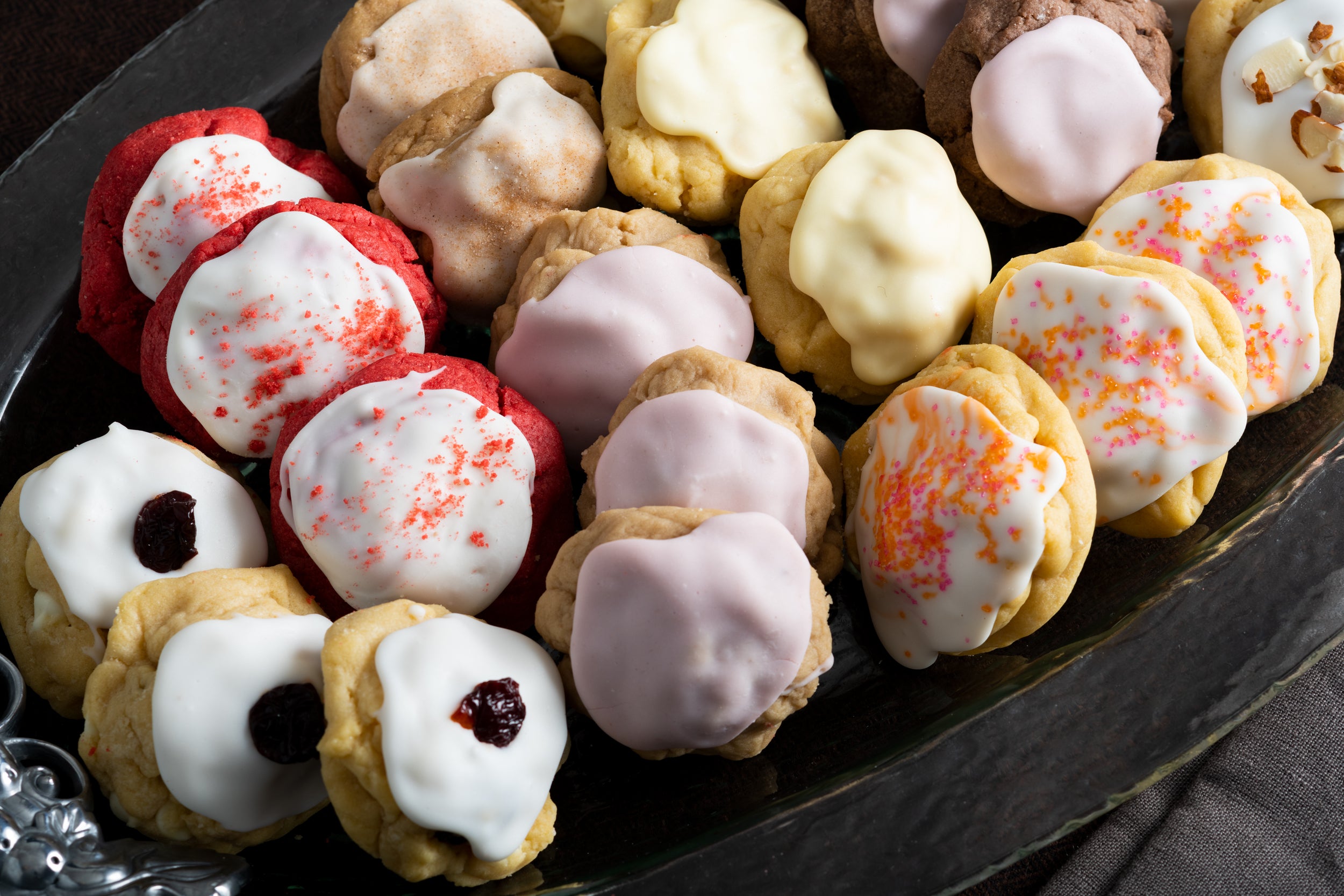 A serving dish filled with a collection of our gourmet, handcrafted iced cookies, featuring White Chocolate Cherry Amaretto, Iced Lemon, Iced Almond, Red Velvet, and Iced Brownie Raspberry.
