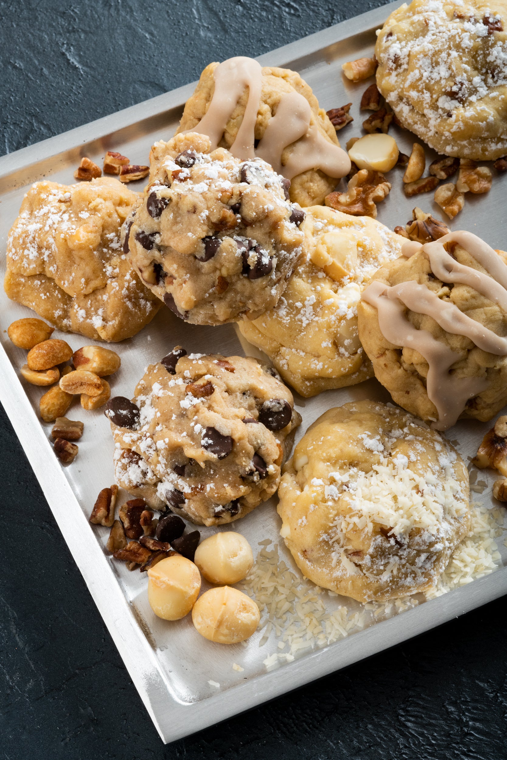 A tray filled with macadamia, iced mapel walnut, chocolate chip cookies, and nuts!
