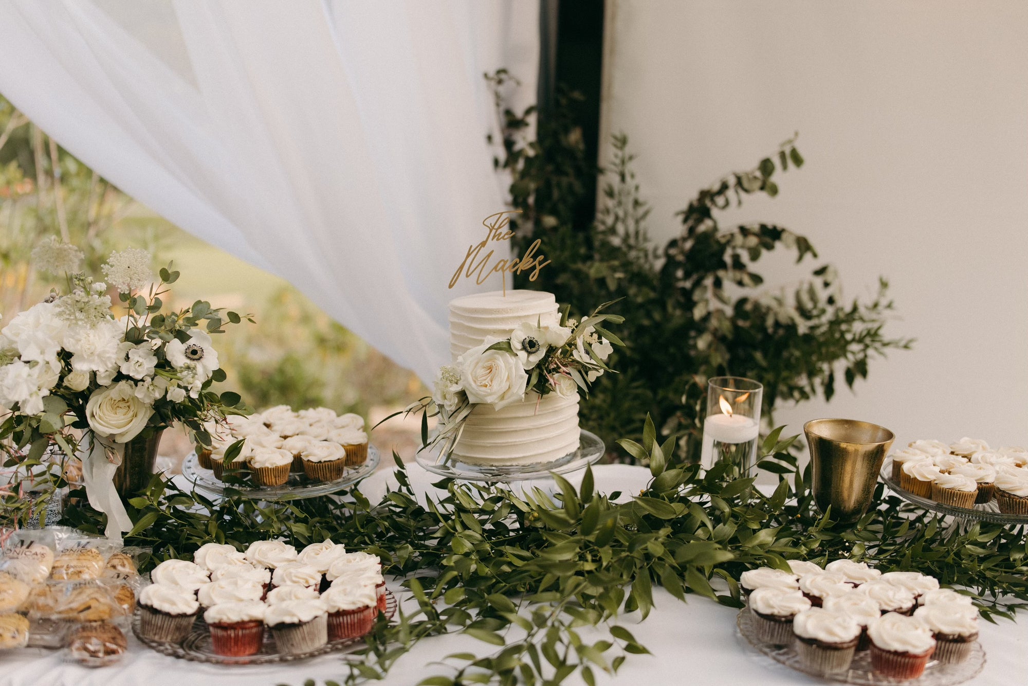 A wedding dessert table featuring a platter of our individually wrapped cookies, wedding cake, and cupcakes.