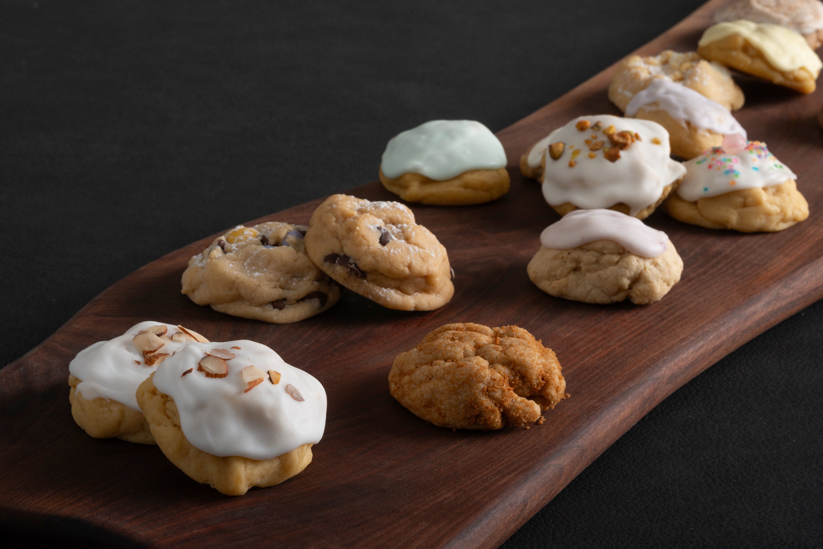 Iced almond, iced keylime, chocolate chip, and royal coronation cookies on a board.
